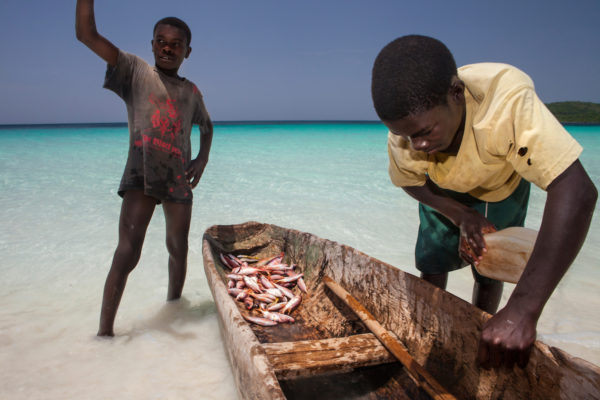 A boy empties the water out of a boat on a beach on Petit Cayemite Island in Haiti